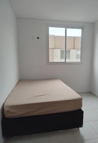 uma cama num quarto branco com uma janela em Quarto privado em Florianópolis