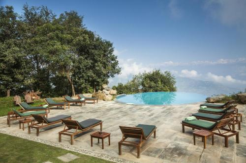 a group of lounge chairs next to a swimming pool at Dwarika's Resort - Dhulikhel in Dhulikhel