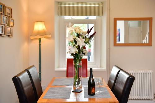 a table with a vase of flowers and a bottle of wine at Rare Free Parking in Heart of the City - Highly Rated Townhouse & Garden - Peaceful Area Less Than 5min Walk to Beach, Shops, Bars, Arena, Marina, Parks in Swansea
