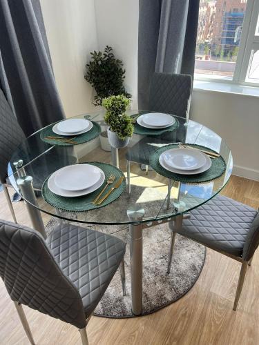 a glass table with two chairs and plates on it at Cosy Centrally Located Flat in Barking
