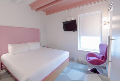 a bedroom with a white bed and a pink chair at The Gallatin in Nashville