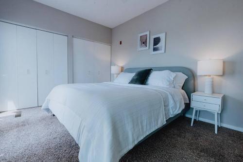 a white bedroom with a large bed and a lamp at Luxe 2BR-1BA Penthouse w Balcony & Pool in Tower Grove