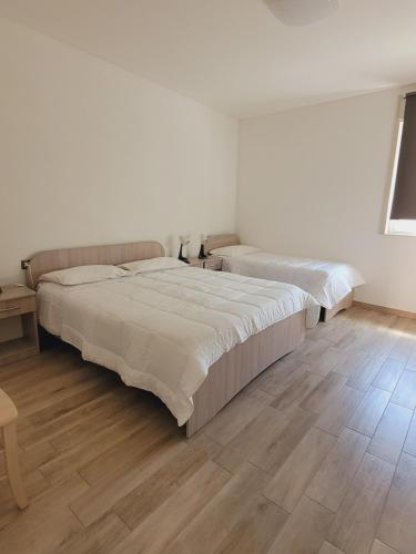 two beds in a white room with wooden floors at HOUSE AIRPORT Catania in Catania
