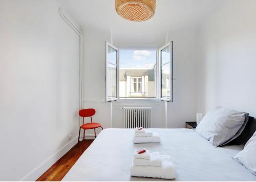 a white bedroom with a bed and a red chair at Appartement, cœur des Batignolles Montmartre in Paris