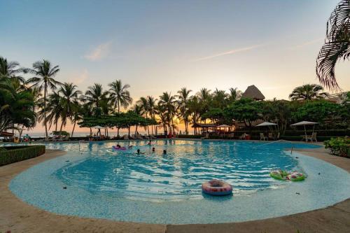 a large pool with people in it with palm trees at Hermosa Palms, Casa Lorenzo Beach Front Club House in Playa Hermosa