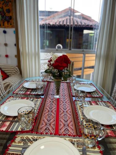 a table with plates and a vase with a red rose at MISKI PUÑUY - Dulces sueños HOSPEDAJE in Cusco
