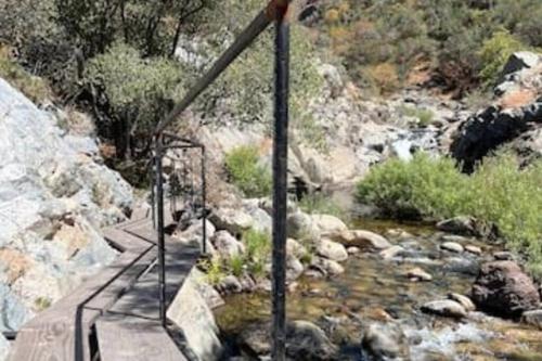 a wooden bridge over a river with rocks and trees at Paradise Ranch Inn- Limitless House Hot Tub,Sauna in Three Rivers