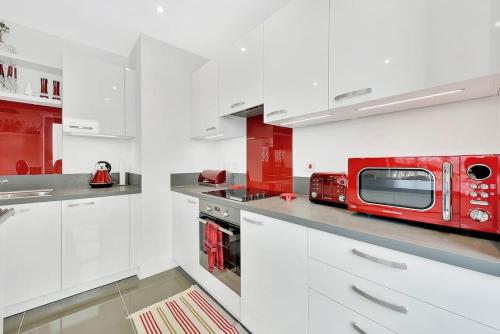 a kitchen with white cabinets and a red microwave at Spacious, Stylish & Secure Apartment in London