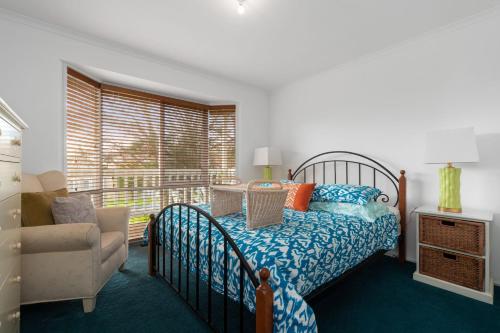 a bedroom with a bed and a chair and a window at Killarney Coastal Cottage in Rye