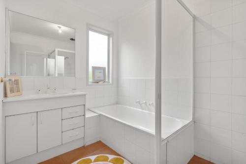 a white bathroom with a tub and a sink at Killarney Coastal Cottage in Rye