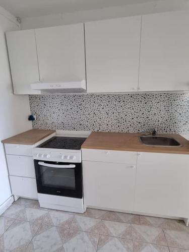 La cuisine est équipée de placards blancs, d'une cuisinière et d'un évier. dans l'établissement Appart Grand Paris Stade France Sites Olympiques, à Pierrefitte-sur-Seine
