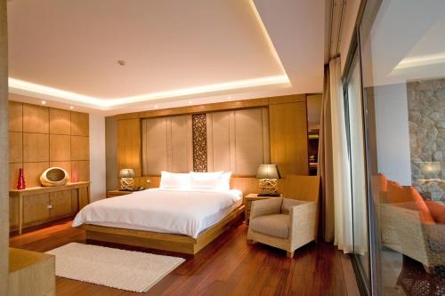 een slaapkamer met een wit bed, een stoel en een bank bij The Nchantra Beachfront Resort in Phuket