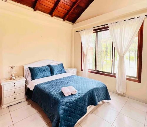 a bedroom with a bed with a blue blanket and a window at Casa de campo acogedora con WIFI- ZONA BBQ- PARQUEO in Loja