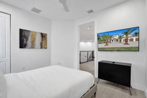 a white bedroom with a bed and a painting on the wall at 5000 Square Ft Beautiful Mansion w 6br Hot Tub Playground Movie Theater & Game Room in Dania Beach