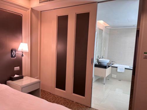 a bedroom with a bed and a bathroom with a sink at Golden Tulip Zhong Xin Hotel Taichung in Taichung