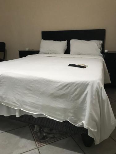 Una cama blanca con control remoto negro. en Good living Guesthouse en Windhoek