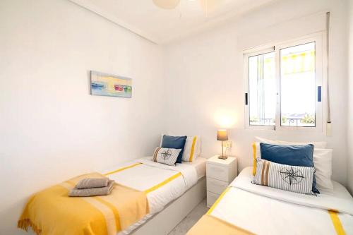 two beds in a white room with a window at PENTHOUSE BELLAVISTA with SEA VIEWS in Torrevieja