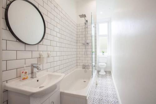 La salle de bains blanche est pourvue d'un lavabo et d'un miroir. dans l'établissement Modern, Light-filled and Sleek West End Apartment, à Glasgow