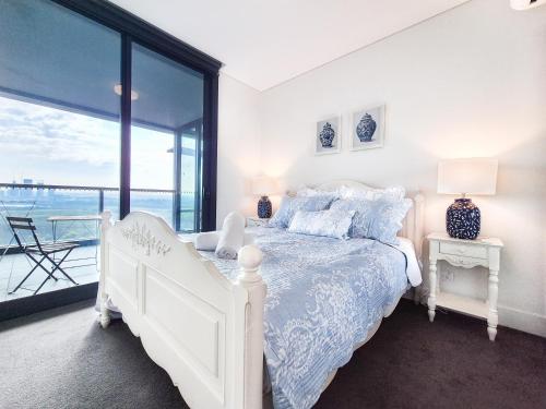 a white bedroom with a white bed and a balcony at Hamptons Style 2BR & kid room w view in Olympic Park in Sydney