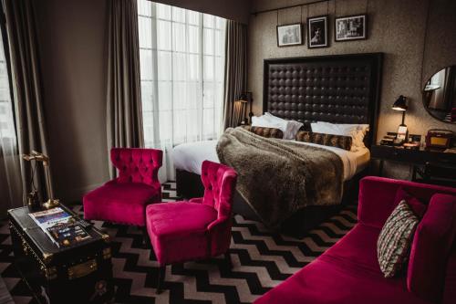 a bedroom with a large bed and two pink chairs at Hotel Gotham in Manchester