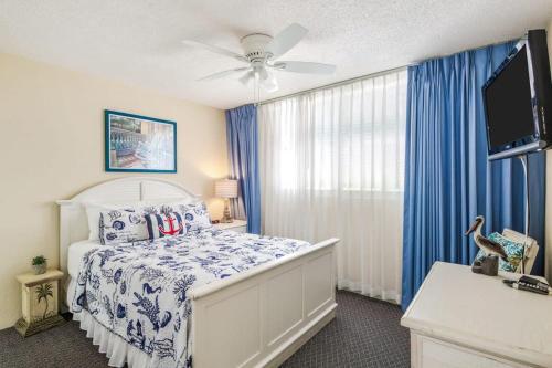 a bedroom with a bed with blue curtains and a tv at The Exuma Cay by Brightwild-Pool View & Parking in Key West