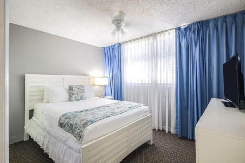 a bedroom with a bed and a window with blue curtains at The Barbados by Brightwild-Bright Condo w Pool in Key West