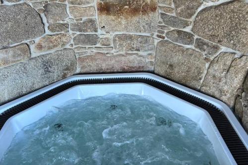 una vasca da bagno riempita d'acqua accanto a un muro di pietra di Casa de Afora Casa con piscina y jacuzzi privados a Santiago de Compostela