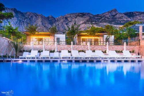 a swimming pool with white chairs and mountains in the background at Poseidon Mobile Home Resort in Makarska