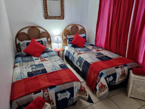 2 bedden in een kleine kamer met rode kussens bij 56 The Bridge St Lucia in St Lucia