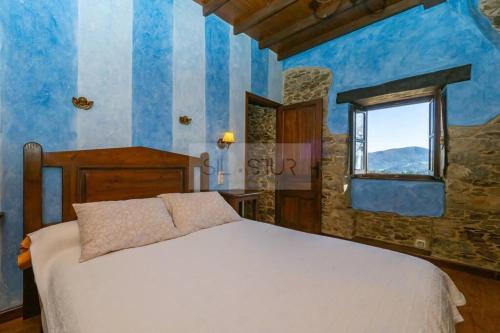 Un dormitorio con una cama con paredes azules y una ventana en La Casona Del Cura III, en Pravia