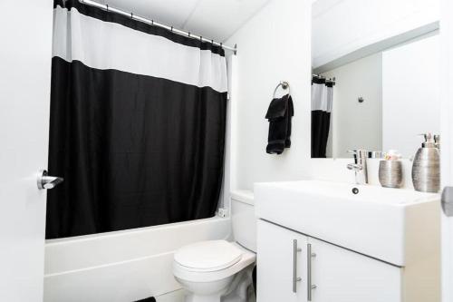 a bathroom with a white toilet and a black shower curtain at Premium 2BD Loft DT Heated Parking Rooftop Patio BBQ Gym Coffee in Winnipeg