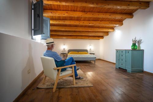un hombre sentado en una silla en una habitación con una cama en Natura Escape in Val di Noto, en Noto