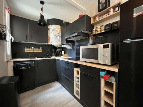 une cuisine avec des armoires noires et un four micro-ondes dans l'établissement Appartement rénové avec 2 pièces et parking privé à Gruissan, proche plage du Grazel - FR-1-229-883, à Gruissan