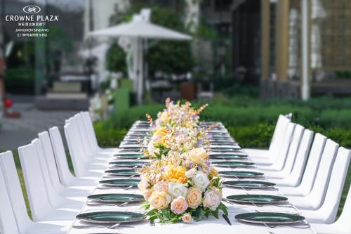 a long table with white chairs and flowers on it at Crowne Plaza Jiangmen Binjiang by IHG in Jiangmen