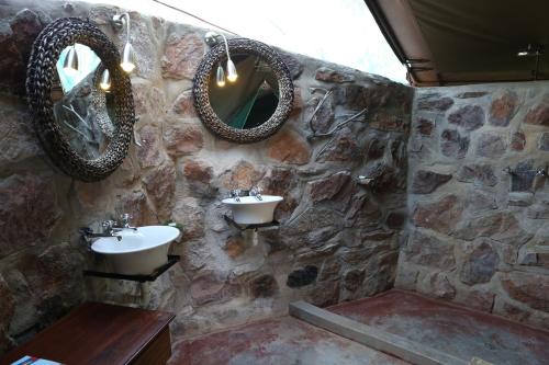 a stone bathroom with two sinks and two mirrors at Epupa Camp in Epupa