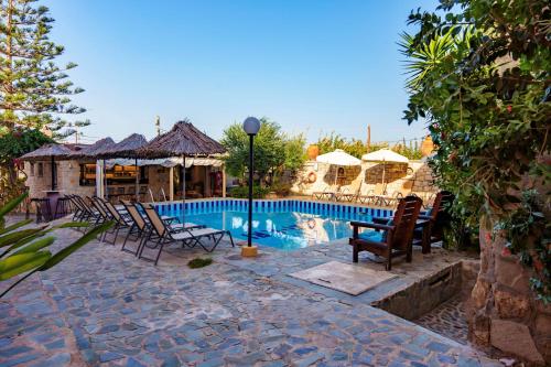 a pool with chairs and umbrellas next to a house at Kri-Kri Village Holiday Apts by Estia in Kokkini Khanion