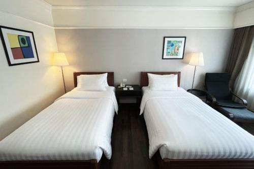 two beds in a hotel room with white sheets at Le Siam Hotel Silom Bangkok by PCL in Bangkok