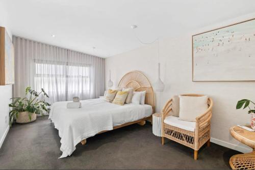 a white bedroom with a large bed and a chair at Whitewash Beachfront Apartment on The Esplanade in Torquay