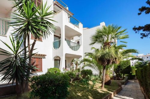 a white building with palm trees in front of it at Flipflop Surfing Playa in Santa Ponsa
