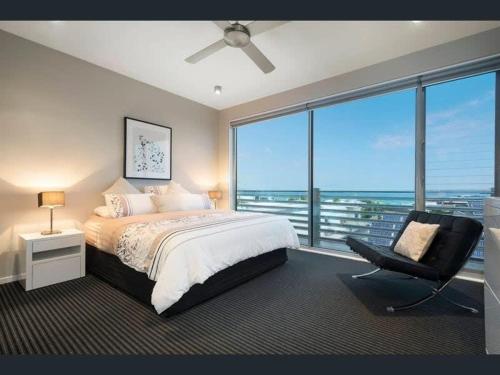 ein Schlafzimmer mit einem Bett und einem Stuhl sowie einem großen Fenster in der Unterkunft Penthouse apartment with breathtaking sea views in Ocean Grove