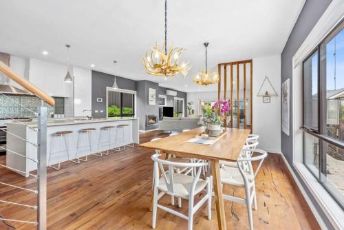 a kitchen with a wooden table and white chairs at Waterways Luxury Poolside Retreat in Prime Location in Ocean Grove