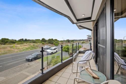 a balcony with a table and chairs and a view of a highway at On The Esplanade - Ocean Front Apartment in Torquay