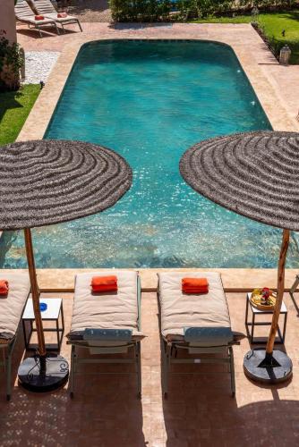 a swimming pool with two lawn chairs and two umbrellas at Villa DAR BOUMA in Ghazoua