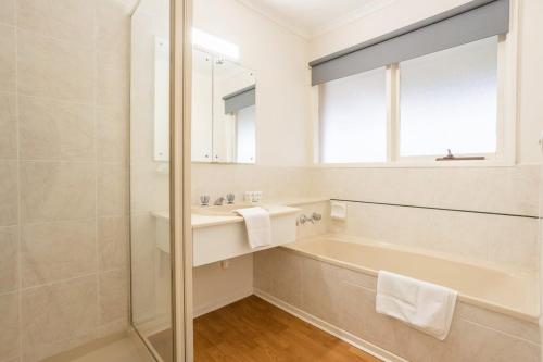 a bathroom with a tub and a sink and a mirror at Cozy Family Friendly Werribee Home in Werribee
