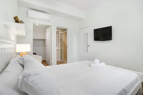 a white bedroom with a white bed and a tv at Elwood Elegance by the Beach in Melbourne