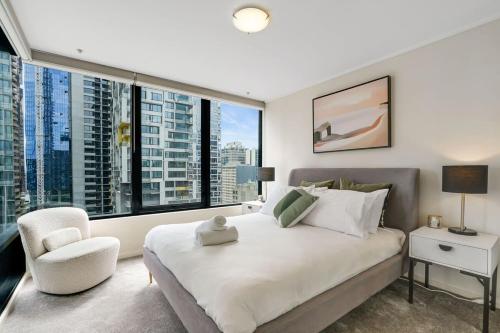 a bedroom with a large bed with a chair and large windows at Spacious&Cozy 2 bedroom City Point Melbourne Apt in Melbourne