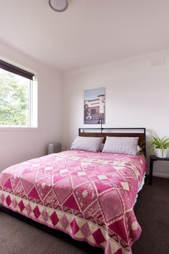 a bedroom with a bed with a pink comforter and a window at Central Classic Collingwood Modern Apt in Melbourne