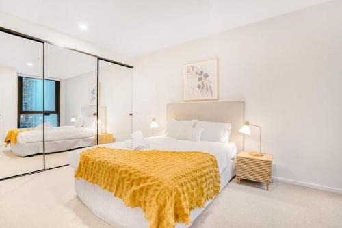 a white bedroom with a large bed with a yellow blanket at Penny Lane - 2BR Apt in the Heart of Moonee Ponds in Melbourne