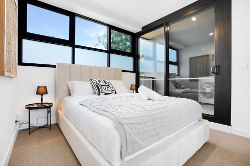a bedroom with a large white bed and large windows at Cozy Nest in Prime Hawthorn w parking & pool in Melbourne