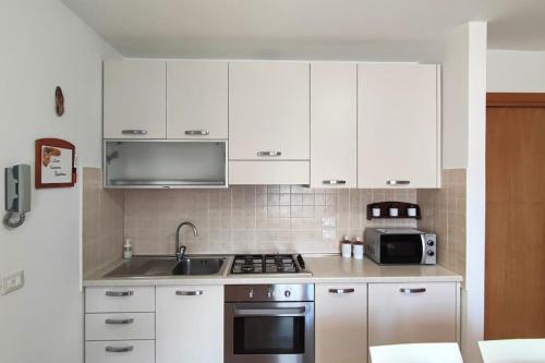 uma cozinha com armários brancos, um lavatório e um micro-ondas em Casa Vacanza Presolana con giardino e box auto em Castione della Presolana